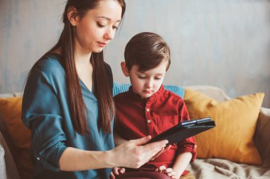 mutlu anne ve yürümeye başlayan çocuk oğlu kullanarak evde tablet. Aile bilgisayar oynarken ya da internet, elektronik cihazlar ve modern yaşamın çocuklarda arama