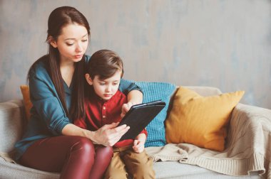 mutlu anne ve yürümeye başlayan çocuk oğlu kullanarak evde tablet. Aile bilgisayar oynarken ya da internet, elektronik cihazlar ve modern yaşamın çocuklarda arama