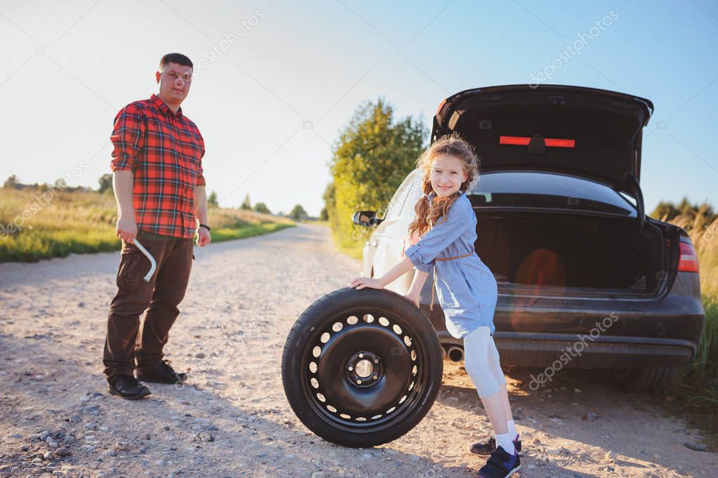 father and daughter changing broken tire during summer rural road trip. Kid helping to fix problems with car