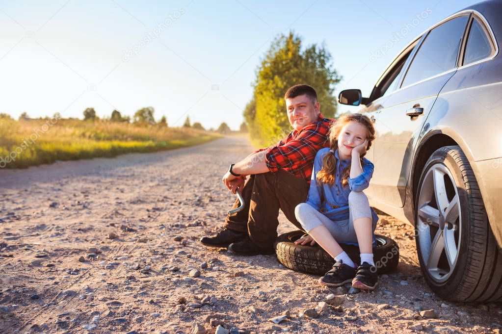 father and daughter changing broken tire during summer rural road trip. Kid helping to fix problems with car