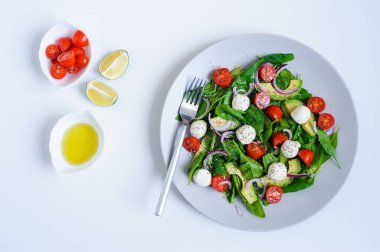 Kiraz domatesli lezzetli diyet salatası, avokado, ıspanak yaprağı, Mozzarella ve beyaz arka planda servis edilen zeytinyağı soslu kırmızı soğan.