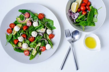Çeri domatesli lezzetli diyet salatası, avokado, ıspanak yaprağı, Mozzarella ve zeytinyağı soslu kırmızı soğan tabakta servis ediliyor.