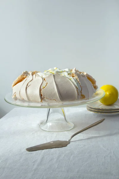 Homemade meringue cake Pavlova with whipped cream and lemon on glass cake stand on the light background