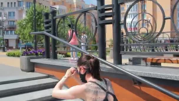 背にタトゥーのある強いスポーティな白人女性黒いマスクで市内公園の階段をジャンプします 接近戦に戻る — ストック動画