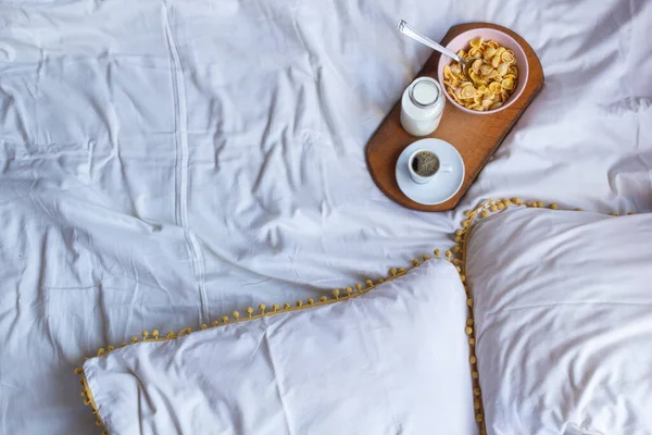 Simple Breakfast in bed with corn flakes, milk and coffe on wooden desk. Yellow and white colors. Flat lay, copy space