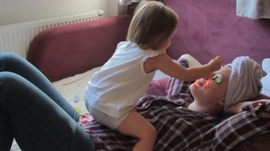 Kadın banyodan sonra gözlerinde salatalıkla rahatlıyor. Küçük kızı annesinin yüzünü turuncu renge boyuyor. Kavram: güzellik, aile, eğlence, rahatla.