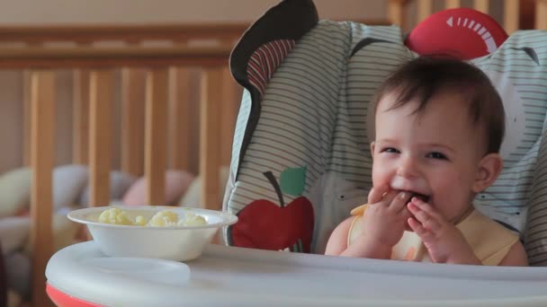 Söt baby äta blomkål första gången hemma. Friska barn näring, Baby första fasta utfodring, baby 7 månader i barnstol äter själv, självmatande — Stockvideo