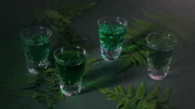Sert alkol. Yeşil apsent ile küçük bardaklar. Orman eğreltiotu ve karanlık arka planda güzel gölgeler.