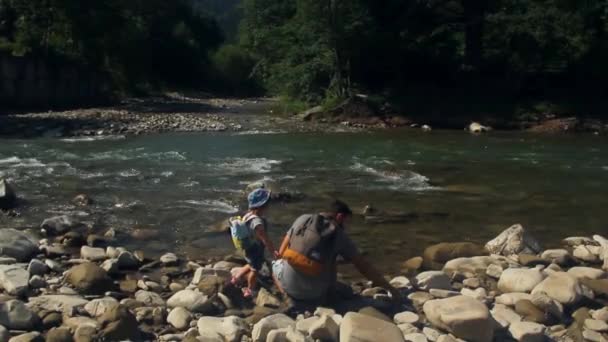 Papá con una hija pequeña está tirando piedras a un río de montaña. Viajar con niños — Vídeos de Stock