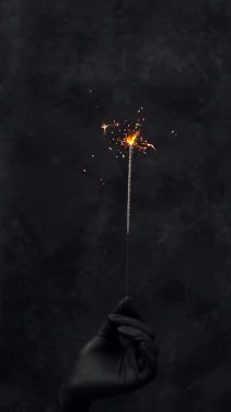 Siyah tıbbi eldivenli bir elin elinde yanan bir maytap var. dikey görünüm yönelimi