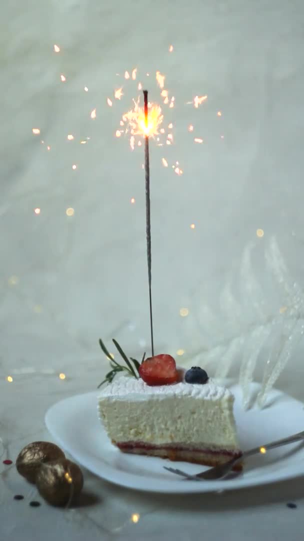 Festliches weißes Kuchenstück mit brennender Wunderkerze auf hellem Hintergrund. vertikale Bildschirmorientierung. — Stockvideo