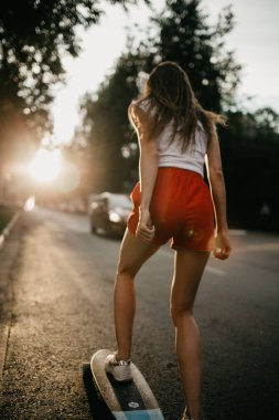 Gün batımında kaykayıyla gezen güzel bir kaykaycı kadın.