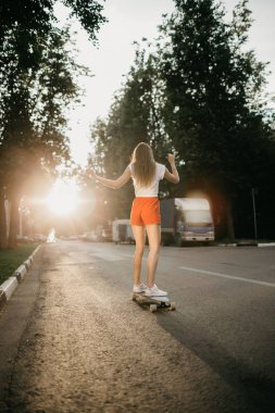 Gün batımında kaykayıyla gezen güzel bir kaykaycı kadın.