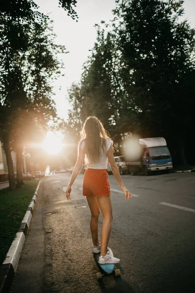 Hermosa mujer de patinaje montando en su palangre en la cit de la puesta del sol. Imagen De Stock