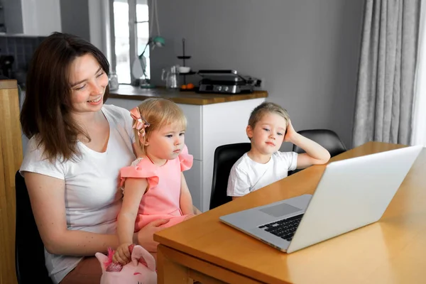 Genç bir oğlu ve kızı olan bir anne dizüstü bilgisayardan eğitim programlarını izliyor.