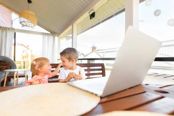 Small smiling kids brother and sister laugh and play laptop, communicate video conference chatting.