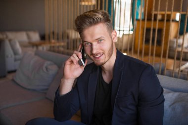 Sarışın, başarılı bir genç adam, modern bir nargile odasında telefonla konuşuyor.