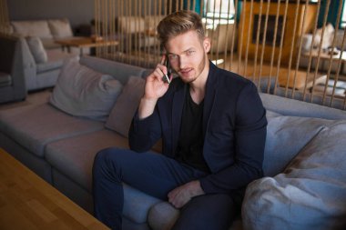 Sarışın, başarılı bir genç adam, modern bir nargile odasında telefonla konuşuyor.