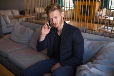 Sarışın, başarılı bir genç adam, modern bir nargile odasında telefonla konuşuyor.