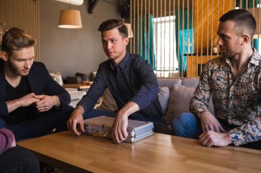 Birkaç adam bir kafede poker oynuyor, ellerinde kartlarla.