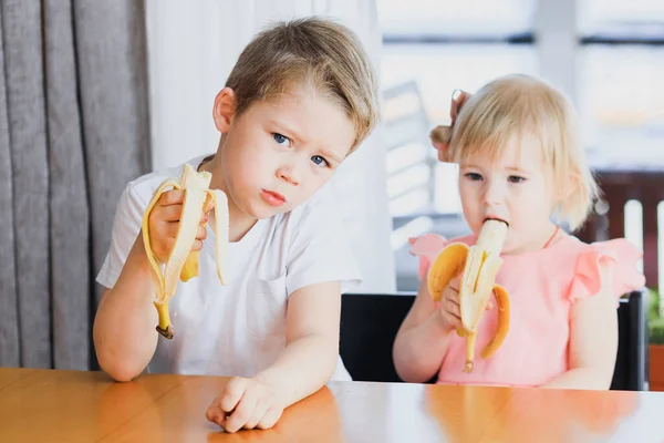 Una niña y un niño comiendo un plátano — Foto de Stock