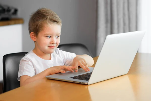 Un niño usando una computadora portátil sentada encima de una mesa en casa Imágenes De Stock Sin Royalties Gratis