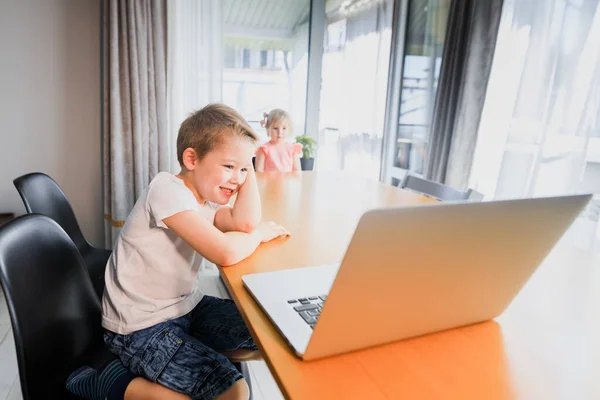 Small smiling kids brother and sister laugh and play laptop, communicate video conference chatting.