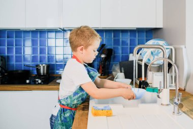 Küçük bir çocuk modern bir mutfakta bulaşık yıkıyor.