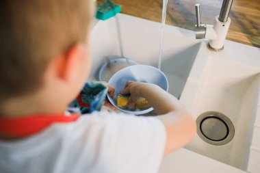 Küçük bir çocuk modern bir mutfakta bulaşık yıkıyor.