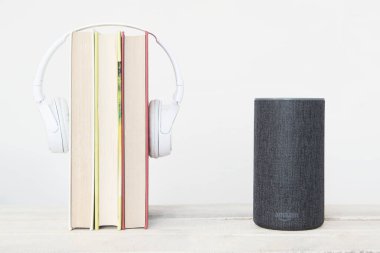 Akıllı konuşmacı Amazon Alexa Echo cihazının yanında beyaz arka planda bazı kitaplar ve kulaklıklar var. Düzenleyicinin metni için boş kopyalama alanı