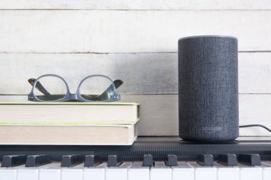 Alexa Echo akıllı hoparlör ve piyanonun yanında ahşap arka planda duran kitaplar için ev otomasyonu. Düzenleyicinin metni için boş kopyalama alanı.