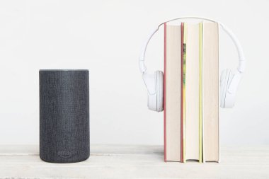 Akıllı konuşmacı Amazon Alexa Echo cihazının yanında beyaz arka planda bazı kitaplar ve kulaklıklar var. Düzenleyicinin metni için boş kopyalama alanı