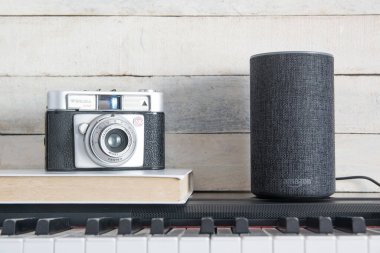Amazon Alexa Echo piyanonun üstünde kamera ve ahşap arka planda bir kitap. Düzenleyicinin metni için boş kopyalama alanı.
