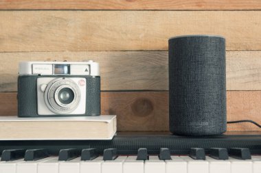 Amazon Alexa Echo piyanonun üstünde kamera ve ahşap arka planda bir kitap. Düzenleyicinin metni için boş kopyalama alanı.