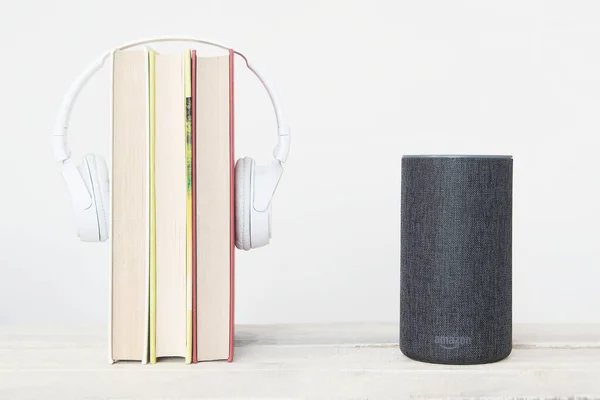 Akıllı konuşmacı Amazon Alexa Echo cihazının yanında beyaz arka planda bazı kitaplar ve kulaklıklar var. Düzenleyicinin metni için boş kopyalama alanı
