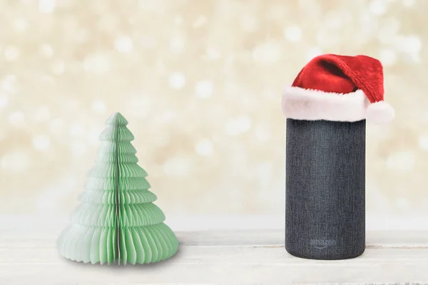 Amazon Alexa Echo akıllı hoparlör cihazı tahtadan bir masanın üzerinde kağıt bir noel ağacının yanında. Düzenleyicinin metni için bokeh arkaplanı ve boş kopya alanı.