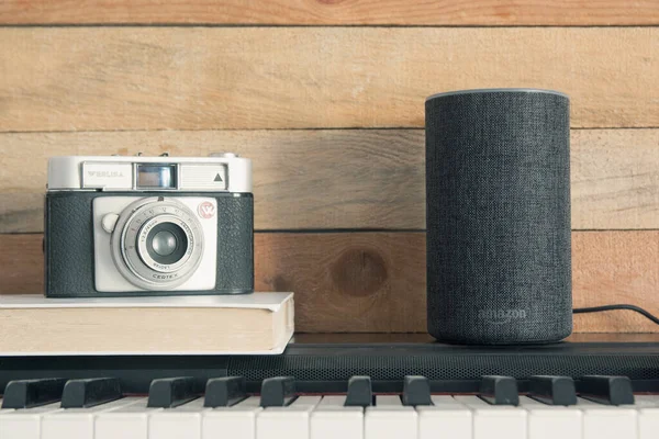 Amazon Alexa Echo piyanonun üstünde kamera ve ahşap arka planda bir kitap. Düzenleyicinin metni için boş kopyalama alanı.