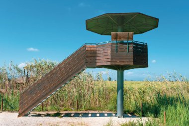 Bird watcher tower in Ebro Delta wetland area with rice field against a cloudy blue sky. Empty copy space for Editor's text clipart