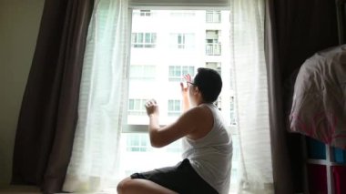 Coronavirus salgınını korumak için sosyal uzaklık kavramı karşı odadaki arkadaşla telefon görüşmesi yaparak apartman dairesinin penceresinden sabah güneşinin tazeliğini geçerek