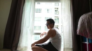 Coronavirus salgınını korumak için sosyal uzaklık kavramı karşı odadaki arkadaşla telefon görüşmesi yaparak apartman dairesinin penceresinden sabah güneşinin tazeliğini geçerek