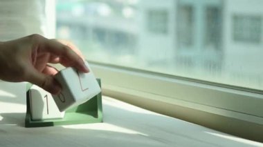 Yeni gün için el değiştiren beyaz ahşap takvim bloğu. Tatlı pembe yatakta, modern pencereden gelen taze sabah ışığı, konsept hayat motivasyonunu başlatır.