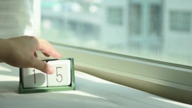 Yeni gün için el değiştiren beyaz ahşap takvim bloğu. Tatlı pembe yatakta, modern pencereden gelen taze sabah ışığı, konsept hayat motivasyonunu başlatır.