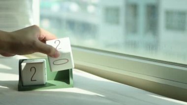 Yeni gün için el değiştiren beyaz ahşap takvim bloğu. Tatlı pembe yatakta, modern pencereden gelen taze sabah ışığı, konsept hayat motivasyonunu başlatır.