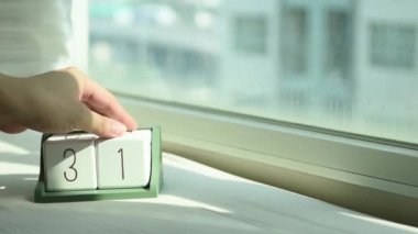 Yeni gün için el değiştiren beyaz ahşap takvim bloğu. Tatlı pembe yatakta, modern pencereden gelen taze sabah ışığı, konsept hayat motivasyonunu başlatır.