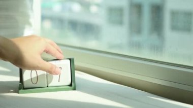 Yeni gün için el değiştiren beyaz ahşap takvim bloğu. Tatlı pembe yatakta, modern pencereden gelen taze sabah ışığı, konsept hayat motivasyonunu başlatır.