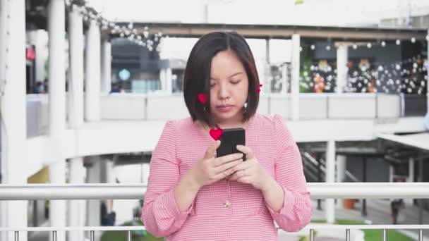 アジアの美しい女性は 画面のソーシャルネットワークから赤いハートアイコンを持つスマートフォンを使用しています 顔マスクなしでソロ屋外をリラックスしますが 社会的距離コロナウイルス新しい通常の概念を維持します 精神的な幸せな健康 — ストック動画