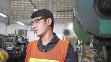 Asyalı mühendis yorgun, dinlenmek için miğfer ve güvenlik gözlüklerini çıkardı. Metal levha fabrikası üretiminde güvenlik üniformasıyla takım molası. Dolly kamera yan görünümü