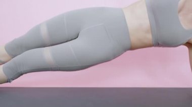 Asyalı kadın yan yatma egzersizi. Çekirdek vücuda odaklanarak seksi altı kaslı kas ve sağlıklı yaşam eğitimi veriyor. Gri spor giyimde güzel bir kadın. Pembe arka planda evde spor ağırlığı çalışması