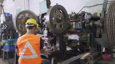 Asyalı işçiler, yarı otomatik beslenme çeliği üreten pul makinesini çalıştırıyor. Metal levha üretim hattında güvenlik üniforması ve miğfer giyiyor.