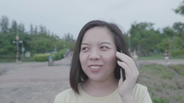 在雨中 亚洲女人和朋友一起在新鲜的室外公园里散步 随风飘扬 随风飘扬 假日穿宽松的黄色T恤 带相机手套 — 图库视频影像